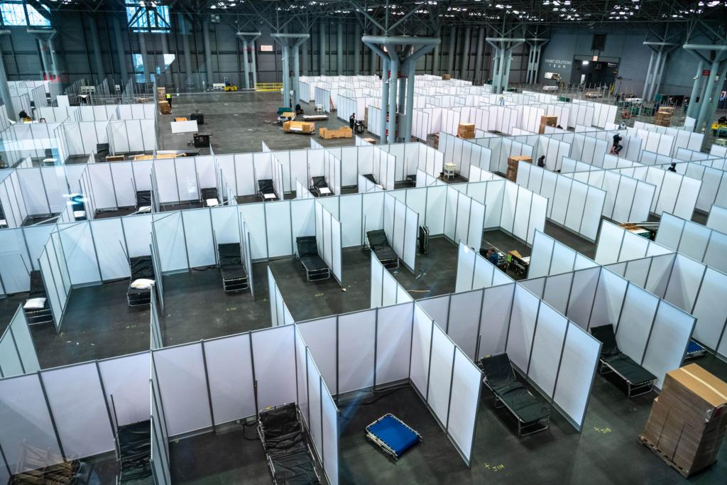 A convention center exhibition hall converted into a hospital with numerous individual examination rooms spread across the floor