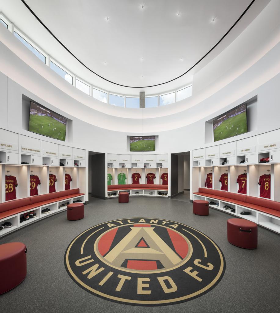 Locker room for a professional soccer team with a large logo in the center and uniforms hung around the room