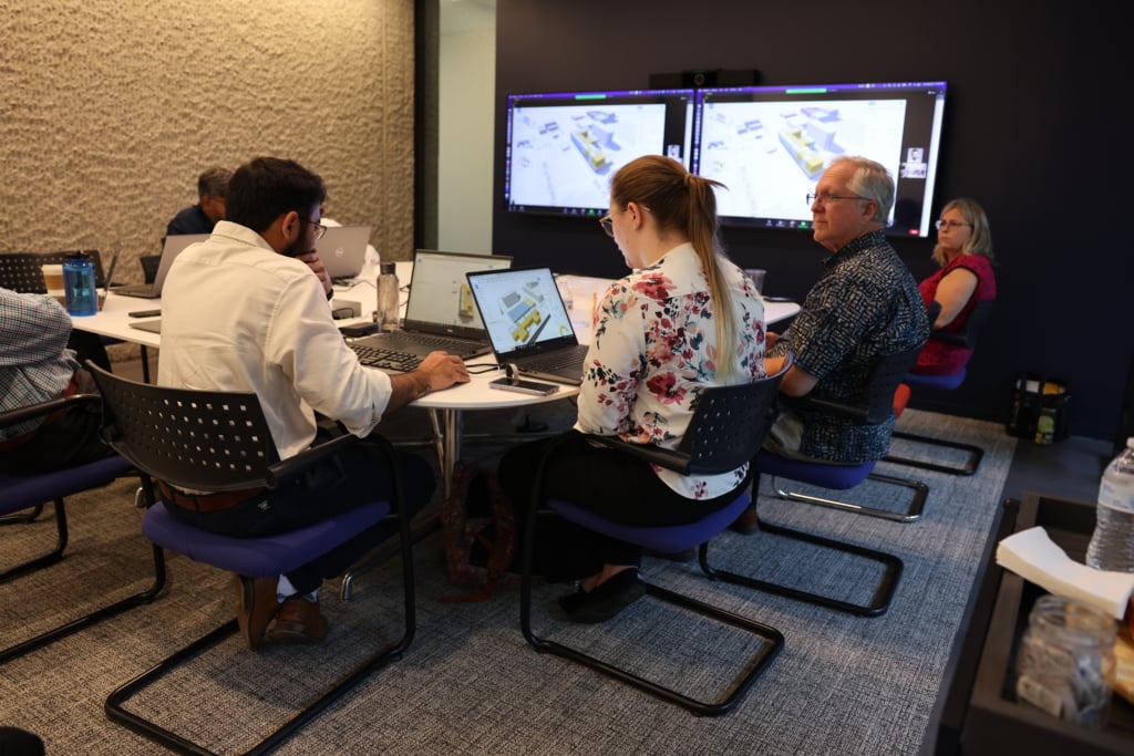 A group of architects sitting around a large conference table. They're at a design charette, experimenting with automation software. 